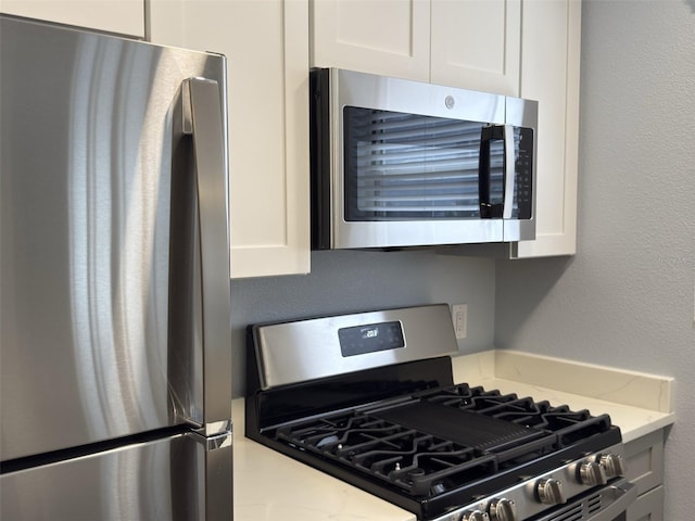 kitchen featuring light stone counters, white cabinetry, stainless steel appliances, and a textured wall