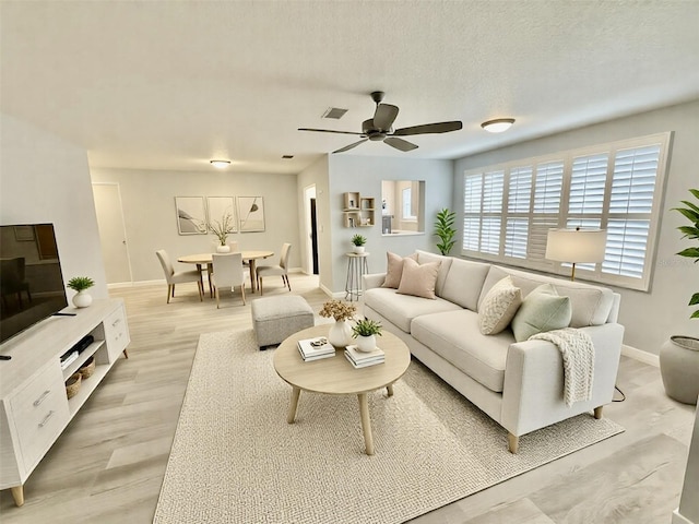 living room featuring baseboards, visible vents, light wood finished floors, ceiling fan, and a textured ceiling