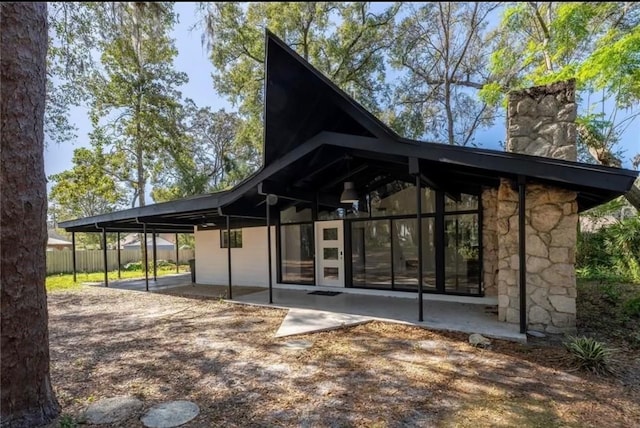 back of property featuring a chimney, a patio area, fence, a carport, and stone siding