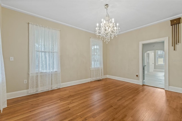 empty room featuring arched walkways, crown molding, wood finished floors, baseboards, and an inviting chandelier