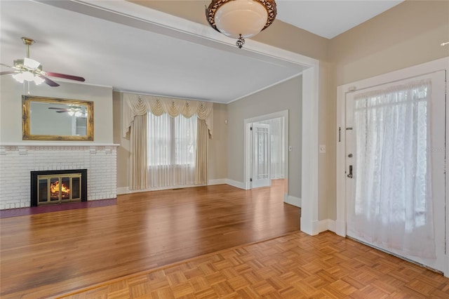 foyer entrance with parquet floors, crown molding, a fireplace, a ceiling fan, and baseboards