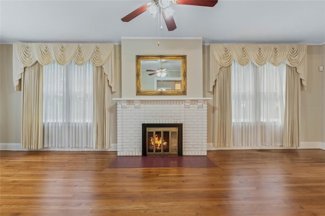 unfurnished living room featuring a ceiling fan, a brick fireplace, baseboards, and wood finished floors