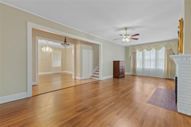 unfurnished living room featuring ceiling fan with notable chandelier, a fireplace, baseboards, and wood finished floors