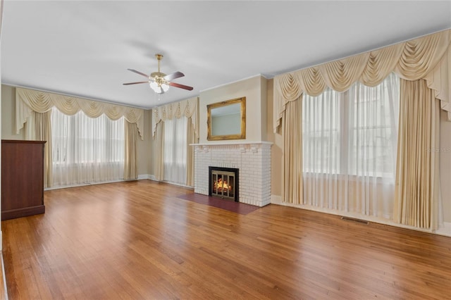 unfurnished living room with a brick fireplace, visible vents, a ceiling fan, and wood finished floors