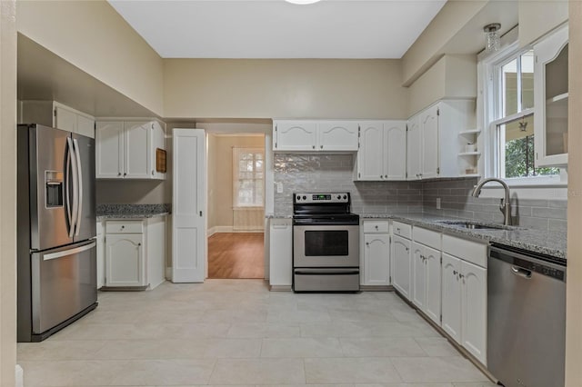 kitchen featuring stainless steel appliances, a sink, white cabinetry, backsplash, and light stone countertops