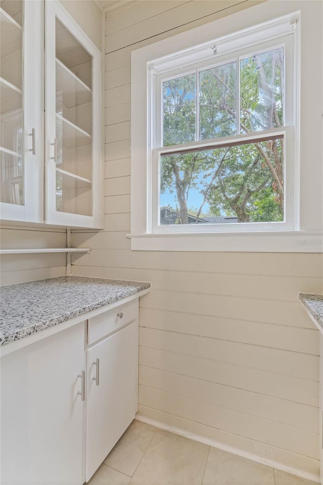 kitchen featuring light stone counters, white cabinetry, wooden walls, and light tile patterned floors