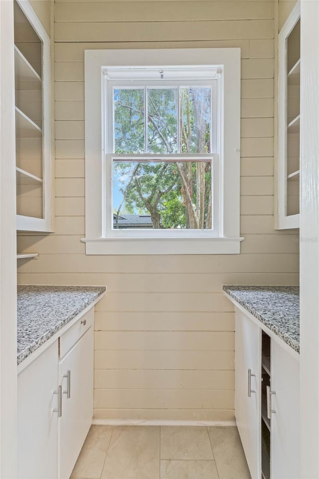 interior space with white cabinetry, light tile patterned floors, wooden walls, and light stone countertops