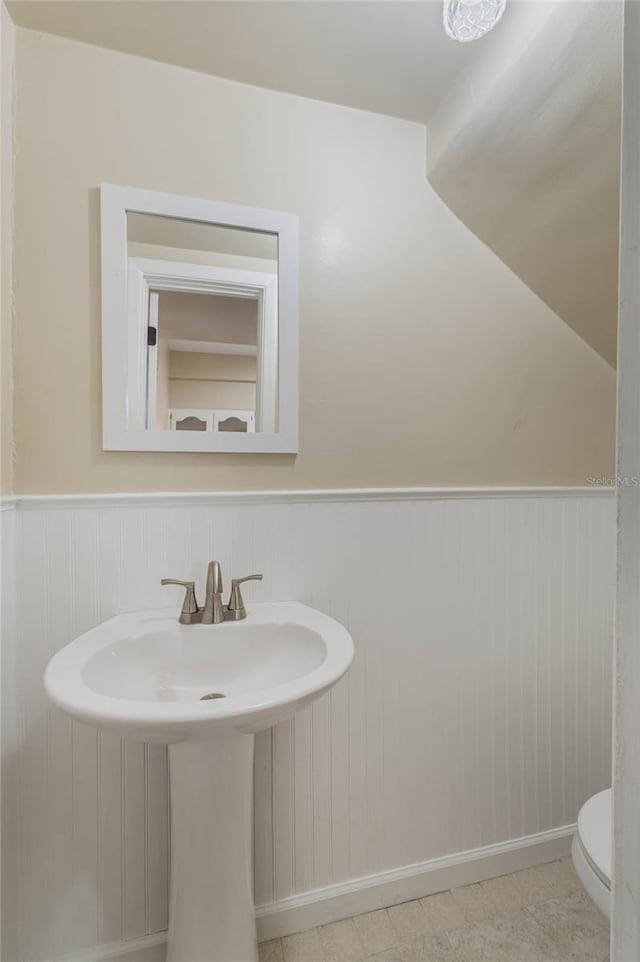 half bathroom featuring wainscoting, a sink, and toilet