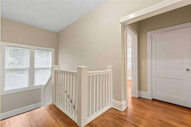 corridor with wood finished floors, an upstairs landing, and baseboards