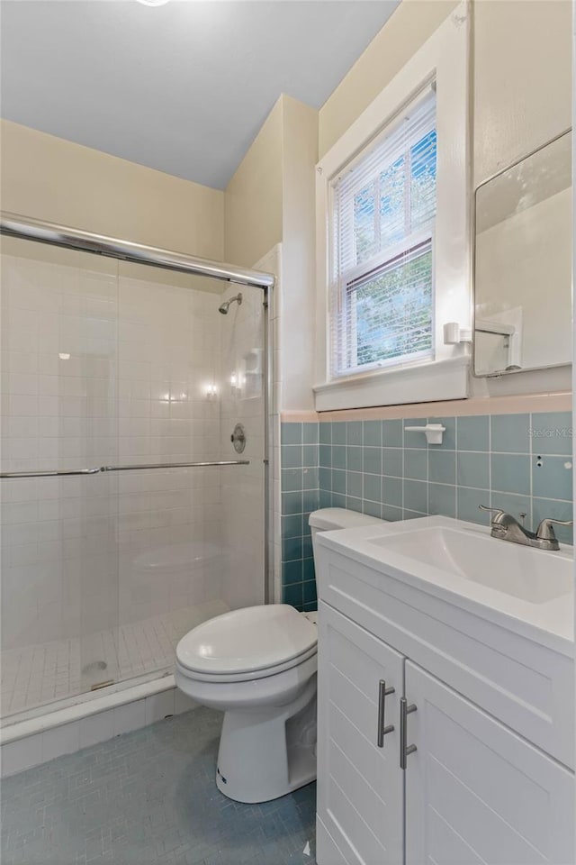 bathroom with toilet, vanity, tile walls, tile patterned floors, and a stall shower