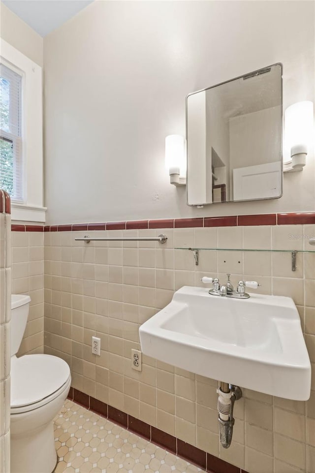 half bathroom with tile walls, toilet, wainscoting, a sink, and tile patterned flooring