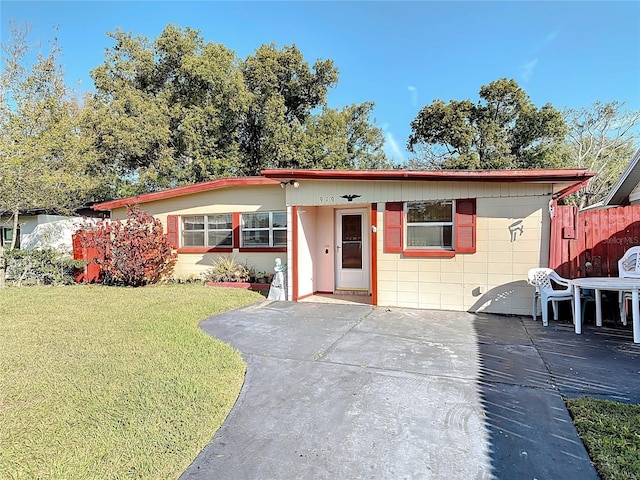 ranch-style house with concrete block siding, fence, a front lawn, and a patio