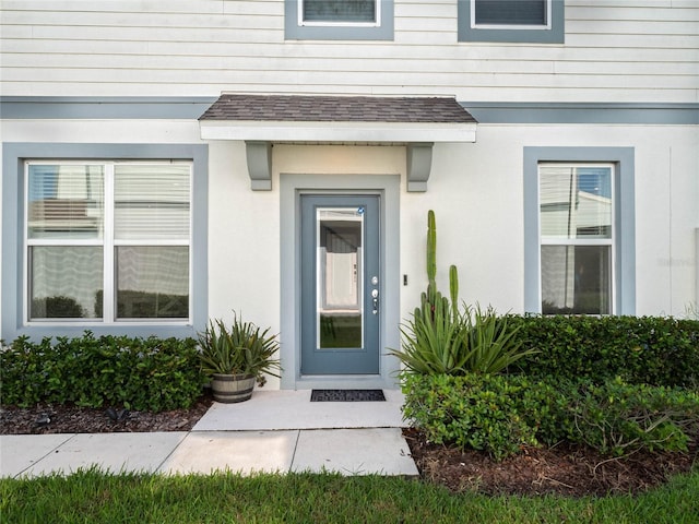 doorway to property featuring stucco siding and a shingled roof