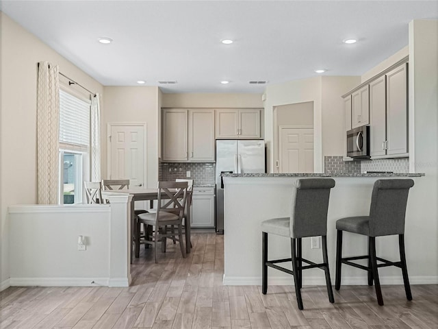 kitchen featuring gray cabinets, a kitchen bar, a peninsula, stainless steel appliances, and visible vents