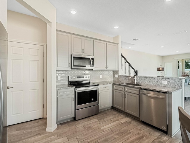 kitchen with a peninsula, stainless steel appliances, tasteful backsplash, a sink, and light wood-style floors