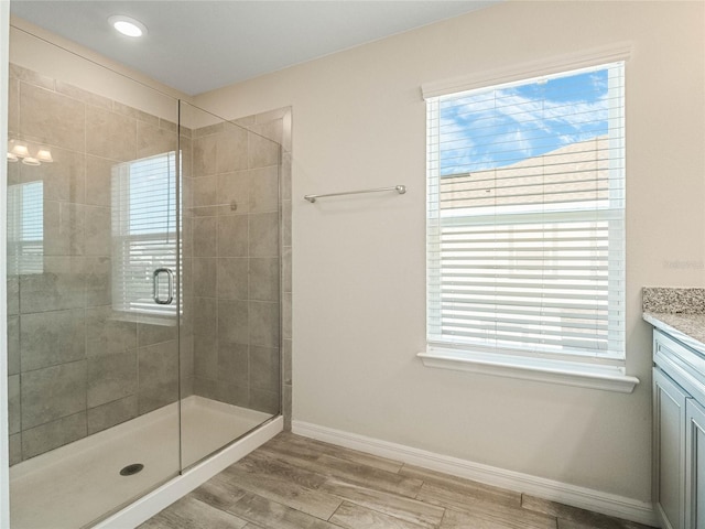 full bath featuring vanity, a stall shower, baseboards, and wood finished floors