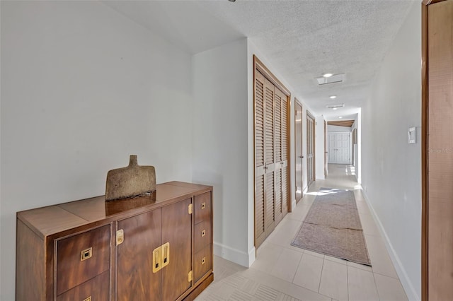 corridor featuring a textured ceiling, light tile patterned floors, and baseboards