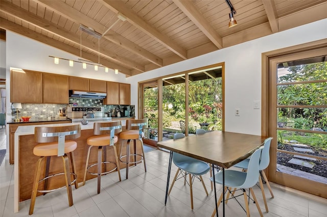 kitchen featuring lofted ceiling with beams, under cabinet range hood, tasteful backsplash, and a healthy amount of sunlight