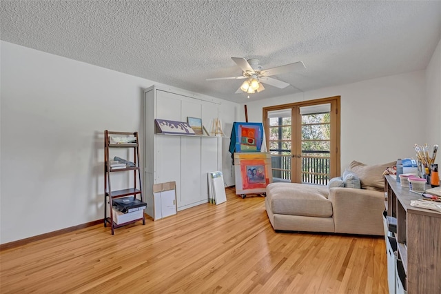 sitting room featuring french doors, light wood-style floors, a ceiling fan, a textured ceiling, and baseboards