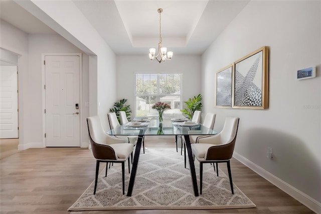 dining room featuring an inviting chandelier, a raised ceiling, baseboards, and wood finished floors