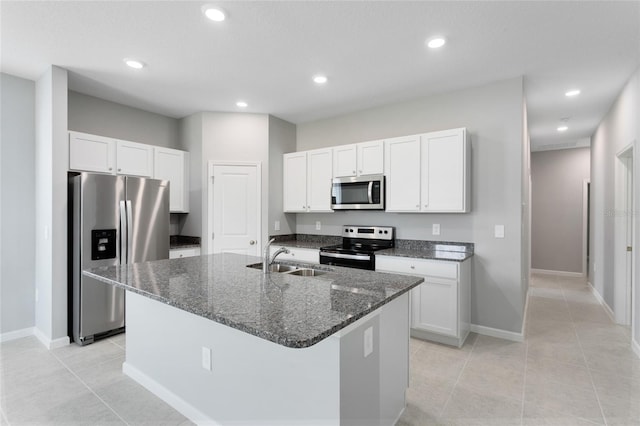 kitchen featuring appliances with stainless steel finishes, white cabinetry, a sink, an island with sink, and dark stone counters