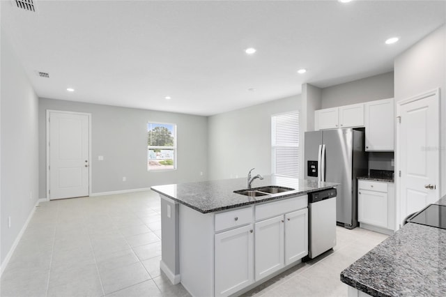 kitchen featuring visible vents, an island with sink, dark stone countertops, stainless steel appliances, and a sink