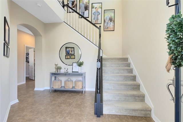 stairs with arched walkways, tile patterned floors, a towering ceiling, and baseboards