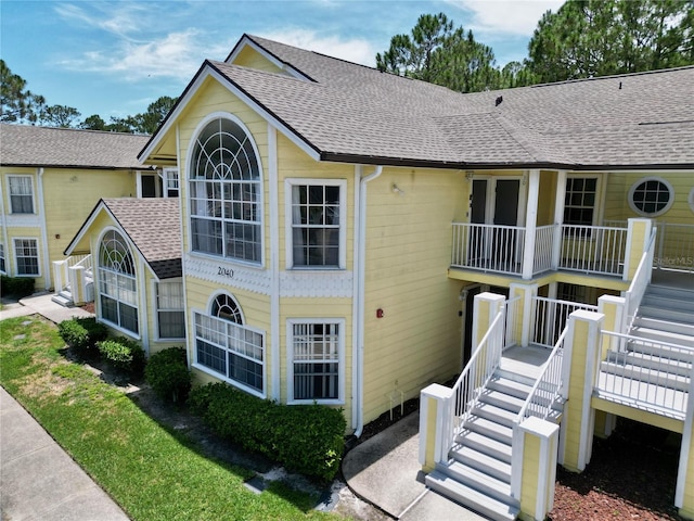 exterior space with stairway, roof with shingles, and a balcony