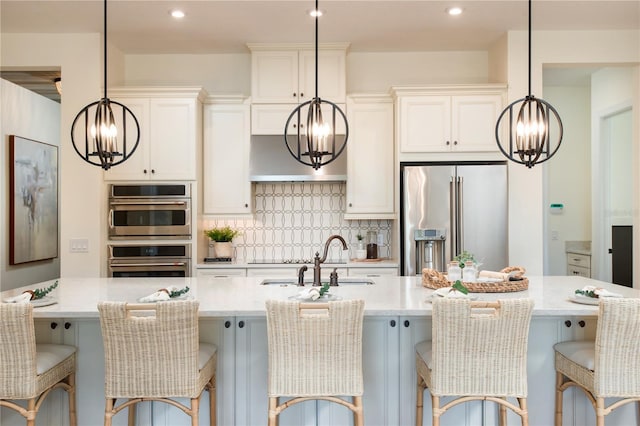 kitchen with stainless steel appliances, a sink, white cabinetry, hanging light fixtures, and backsplash