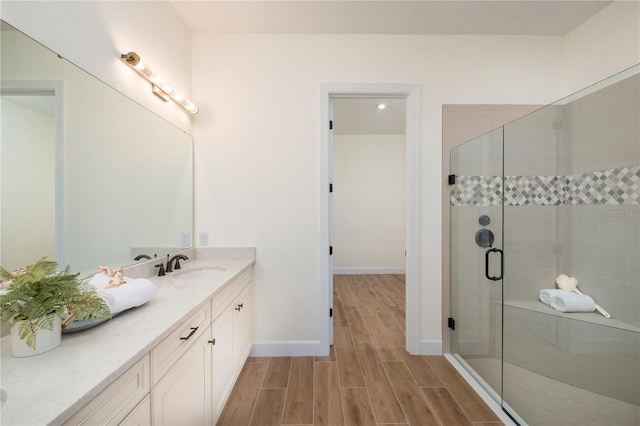 full bathroom featuring wood tiled floor, vanity, baseboards, and a shower stall