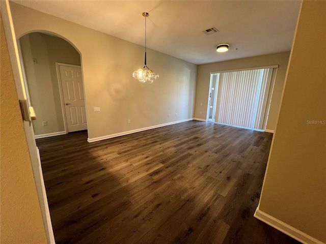 spare room with arched walkways, dark wood-style flooring, visible vents, and baseboards