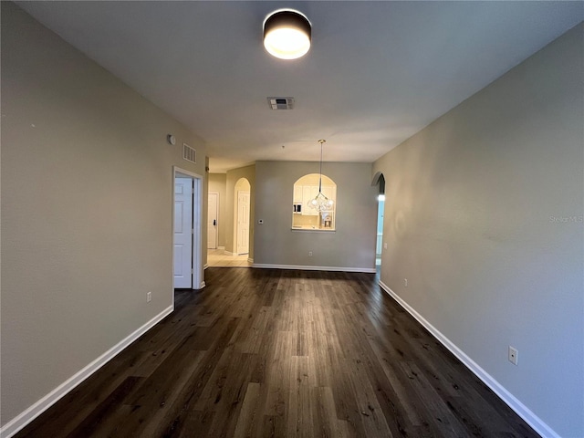 unfurnished dining area featuring visible vents, arched walkways, dark wood-type flooring, and baseboards