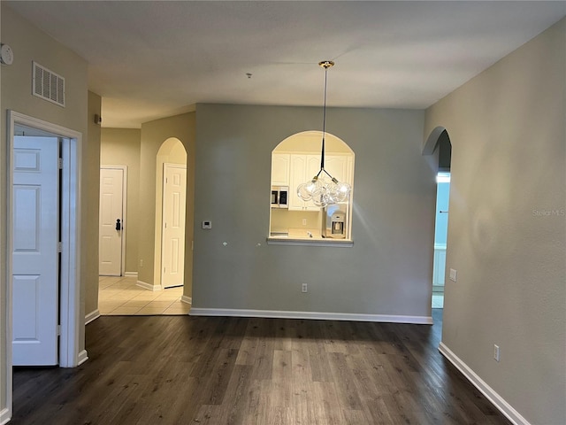 unfurnished dining area with baseboards, visible vents, dark wood finished floors, and arched walkways