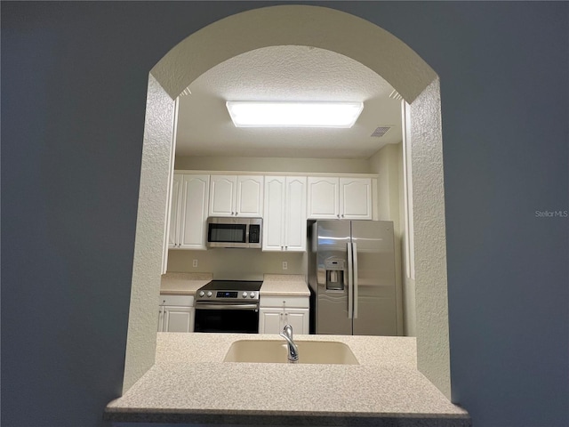 kitchen with a textured wall, stainless steel appliances, a sink, and visible vents