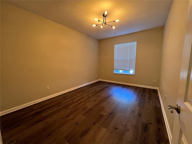 empty room with baseboards, dark wood-type flooring, a textured ceiling, and a notable chandelier