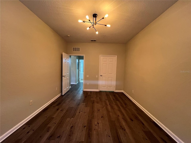 unfurnished room featuring visible vents, dark wood-type flooring, a textured ceiling, a chandelier, and baseboards