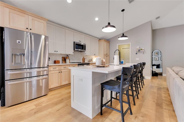 kitchen with a center island with sink, tasteful backsplash, lofted ceiling, light countertops, and appliances with stainless steel finishes