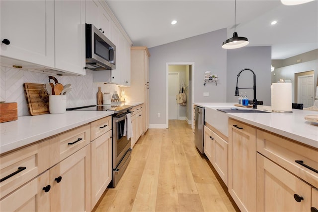 kitchen with lofted ceiling, stainless steel appliances, light brown cabinetry, and a sink