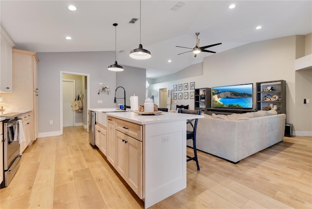 kitchen featuring a breakfast bar area, light wood finished floors, light countertops, stainless steel dishwasher, and a kitchen island with sink