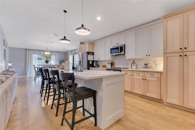 kitchen featuring light countertops, decorative backsplash, light brown cabinetry, appliances with stainless steel finishes, and an island with sink