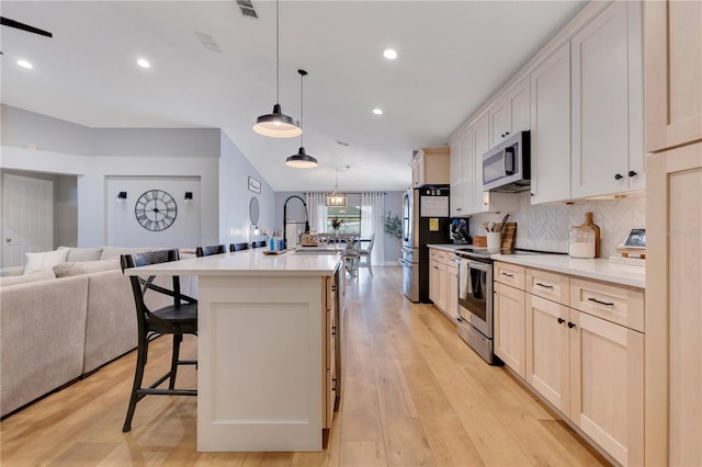 kitchen featuring decorative backsplash, an island with sink, appliances with stainless steel finishes, a breakfast bar, and open floor plan