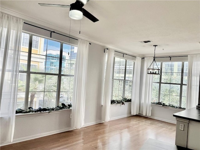 doorway with ceiling fan, wood finished floors, visible vents, baseboards, and ornamental molding