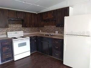 kitchen featuring dark brown cabinetry, white appliances, decorative backsplash, dark wood-style floors, and a sink