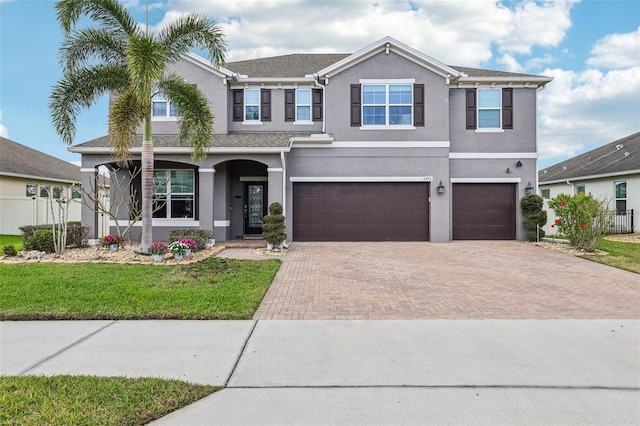 view of front facade featuring a garage, fence, decorative driveway, stucco siding, and a front lawn