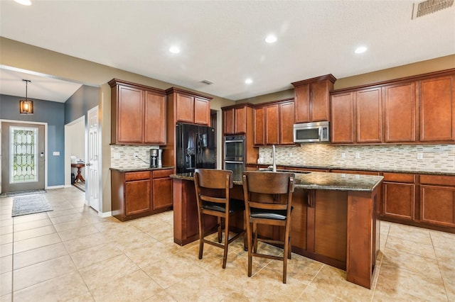 kitchen with a breakfast bar area, a sink, visible vents, appliances with stainless steel finishes, and a center island with sink