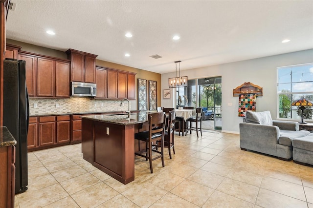 kitchen with stainless steel microwave, backsplash, freestanding refrigerator, open floor plan, and a sink