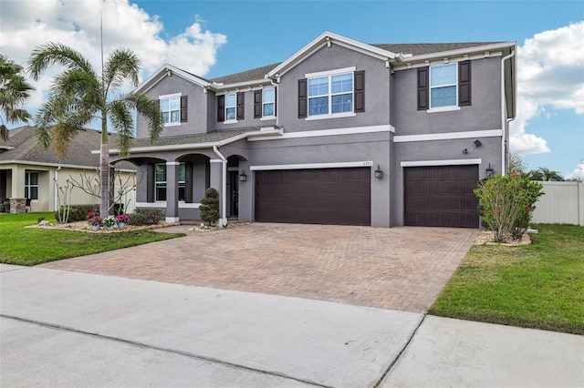 view of front of home featuring a garage, a front lawn, decorative driveway, and stucco siding