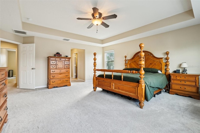 bedroom featuring a tray ceiling, a ceiling fan, visible vents, and light colored carpet