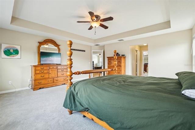 carpeted bedroom featuring a tray ceiling, visible vents, connected bathroom, and baseboards