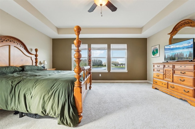 carpeted bedroom featuring ceiling fan, a raised ceiling, and baseboards